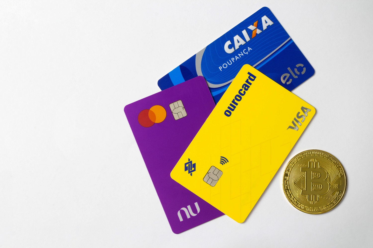 三张巴西银行卡旁边是一枚代表比特币的金属硬币。